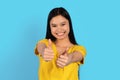 Cheerful pretty young chinese woman in yellow t-shirt showing thumbs up gesture, recommend ad