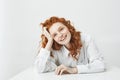 Cheerful pretty young girl with foxy hair smiling laughing sitting at table over white background.