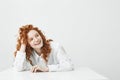 Cheerful pretty young girl with foxy hair smiling laughing sitting at table over white background.