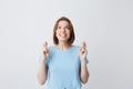 Cheerful pretty young woman in blue tshirt with fingers crossed looking up and wishing for happiness isolated over white Royalty Free Stock Photo