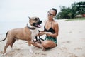 Cheerful asian young woman in eyeglases sitting and hugging her dog on the beach Royalty Free Stock Photo