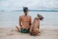 Cheerful asian young woman in eyeglases sitting and hugging her dog on the beach Royalty Free Stock Photo