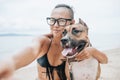 Cheerful asian young woman in eyeglases sitting and doing sekfie with her dog on the beach Royalty Free Stock Photo