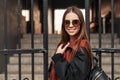 Cheerful pretty young woman hipster in stylish sunglasses in trendy casual youth clothes with leather backpack on a walk. Portrait Royalty Free Stock Photo