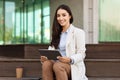 Cheerful pretty young woman secretary manager in suit, write at clipboard work with documents, in city