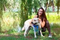 Cheerful pretty young woman sitting and hugging her dog at river bank in park Royalty Free Stock Photo