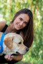 Cheerful pretty young woman sitting and hugging her dog at river bank in park Royalty Free Stock Photo