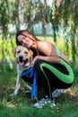 Cheerful pretty young woman sitting and hugging her dog at river bank Royalty Free Stock Photo