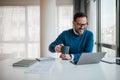 Cheerful professional enjoying coffee while working on laptop at office desk