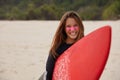 Cheerful professional young female surfer smiles broadly, carries red waxed surfboard, has zinc on face, happy after Royalty Free Stock Photo