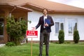 Cheerful property manager showing FOR SALE sign near country house Royalty Free Stock Photo