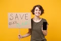 Cheerful protesting woman hold protest broadsheet placard mobile phone with blank empty screen isolated on yellow