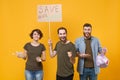 Cheerful protesting young three people hold protest broadsheet placard plastic bottles trash bag isolated on yellow