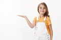 Cheerful proud cute little girl showing achievement, introduce cool copy space, raise hand hold something on blank space