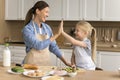 Cheerful proud mom teaching adorable little kid girl to cook
