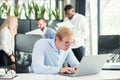 Cheerful purposeful male office worker with funny eyeglasses sits at his workplace and using laptop to solve financial