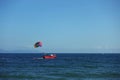 Cheerful red boat sails across a tranquil blue ocean, a colorful parachute soaring