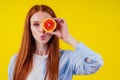 Cheerful, redhaired ginger woman holding red hybrid orange in studio yellow background,autumn vitamin immunity concept