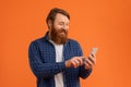 Cheerful redhaired man with beard smiles at his phone, studio