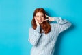 Cheerful redhead female model sending good vibes, smiling and showing peace sign, standing over blue background Royalty Free Stock Photo