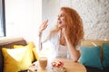 Cheerful redhead young lady sitting in cafe while eating dessert. Royalty Free Stock Photo