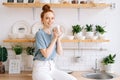 Cheerful redhead young woman holding cup of hot coffee while standing in kitchen room. Royalty Free Stock Photo