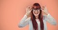 Cheerful redheaded female hipster wearing eyeglasses against orange background