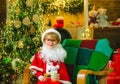 Cheerful Santa Claus child holding glass with milk and cookie with fireplace and Christmas Tree in the background. Royalty Free Stock Photo