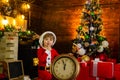 Cheerful Santa Elf kid holding clock. Check contents of christmas stocking. Christmas gifts. Family holiday. Holiday. It Royalty Free Stock Photo