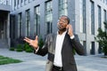 Cheerful and satisfied african american boss outside office building smiling and talking to colleagues on phone, man in Royalty Free Stock Photo