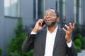Cheerful and satisfied african american boss outside office building smiling and talking to colleagues on phone, man in Royalty Free Stock Photo