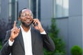 Cheerful and satisfied african american boss outside office building smiling and talking to colleagues on phone, man in Royalty Free Stock Photo