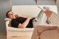 Cheerful satisfied young man in casual clothing laying on couch at counselor office, talking with therapist woman, pleasant Royalty Free Stock Photo