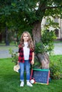 Cheerful school girl holds stack of books in garden near school. Preschool education. Back to school. smiling little girl sit on g Royalty Free Stock Photo