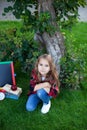 Cheerful school girl holds stack of books in garden near school. Preschool education. Back to school. smiling little girl sit on g Royalty Free Stock Photo