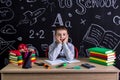 Cheerful schoolboy sitting on the desk with books, school supplies, with both arms under the cheecks