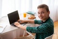 Cheerful schooler having break from studying, typing on laptop