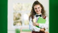 Cheerful schoolgirl in school uniform standing in the hallway with books