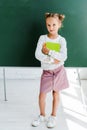 cheerful schoolkid holding books near green chalkboard in classroom .