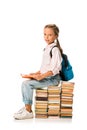 cheerful schoolkid sitting on books and looking at camera on white.