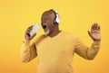 Cheerful senior black man listening to music in wireless headphones, singing, using smartphone as microphone, mockup Royalty Free Stock Photo