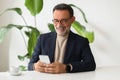 Cheerful senior businessman in a smart blazer browsing on his smartphone