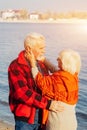 Cheerful senior citizens woman and man are standing and hugging on the lake, against the background of the bridge Royalty Free Stock Photo