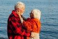 Cheerful senior citizens woman and man are standing and hugging on the lake, against the background of the bridge Royalty Free Stock Photo