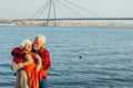 Cheerful senior citizens woman and man are standing and hugging on the lake, against the background of the bridge