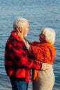 Cheerful senior citizens woman and man are standing and hugging on the lake, against the background of the bridge Royalty Free Stock Photo