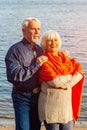 Cheerful senior citizens woman and man are standing and hugging on the lake, against the background of the bridge Royalty Free Stock Photo