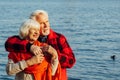 Cheerful senior citizens woman and man are standing and hugging on the lake, against the background of the bridge Royalty Free Stock Photo