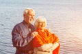 Cheerful senior citizens woman and man are standing and hugging on the lake, against the background of the bridge