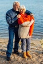 Cheerful senior citizens woman and man are standing and hugging on the lake, against the background of the bridge Royalty Free Stock Photo